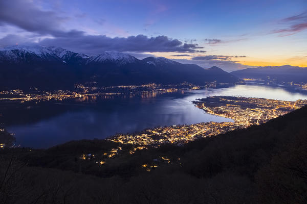 View of the blue hour and city lights over Locarno, Ascona and Lago Maggiore from the trail to Monti di Lego. Mergoscia, Valle Verzasca, Canton Ticino, Switzerland.