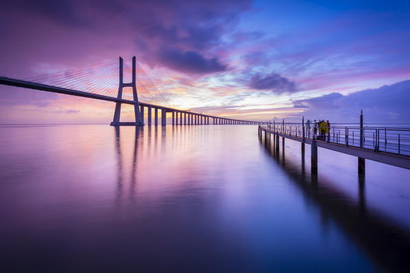 A colorful sunrise behind the Vasco da Gama bridge, reflected on the Tagus River. Lisbon, Portugal, Europe.