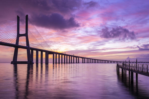 A colorful sunrise behind the Vasco da Gama bridge, reflected on the Tagus River. Lisbon, Portugal, Europe.
