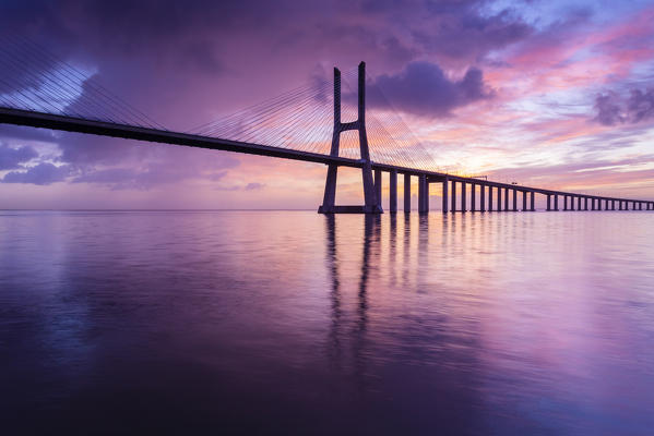 A colorful sunrise behind the Vasco da Gama bridge, reflected on the Tagus River. Lisbon, Portugal, Europe.