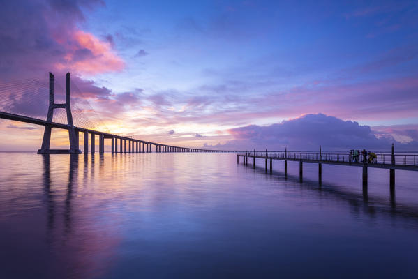 A colorful sunrise behind the Vasco da Gama bridge, reflected on the Tagus River. Lisbon, Portugal, Europe.