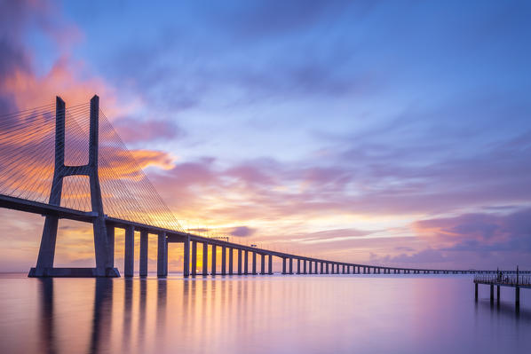 A colorful sunrise behind the Vasco da Gama bridge, reflected on the Tagus River. Lisbon, Portugal, Europe.