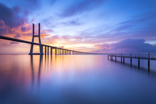 A colorful sunrise behind the Vasco da Gama bridge, reflected on the Tagus River. Lisbon, Portugal, Europe.