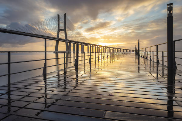 A colorful sunrise behind the Vasco da Gama bridge, reflected on the Tagus River. Lisbon, Portugal, Europe.