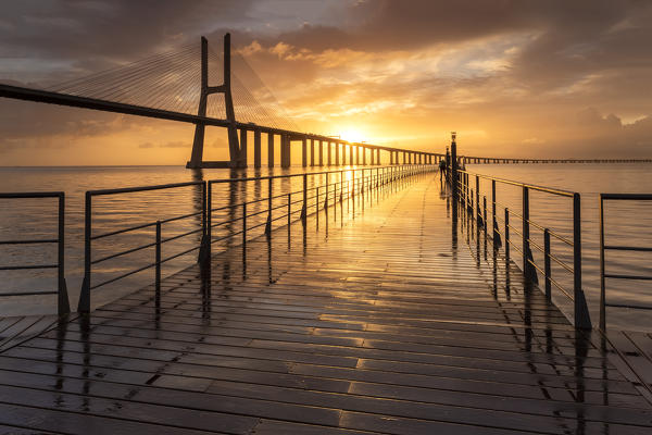 A colorful sunrise behind the Vasco da Gama bridge, reflected on the Tagus River. Lisbon, Portugal, Europe.