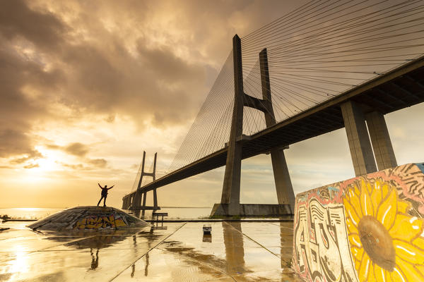 A person enjoying a colorful sunrise at the Skatepark Expo, in front of the Vasco da Gama bridge. Lisbon, Portugal, Europe.