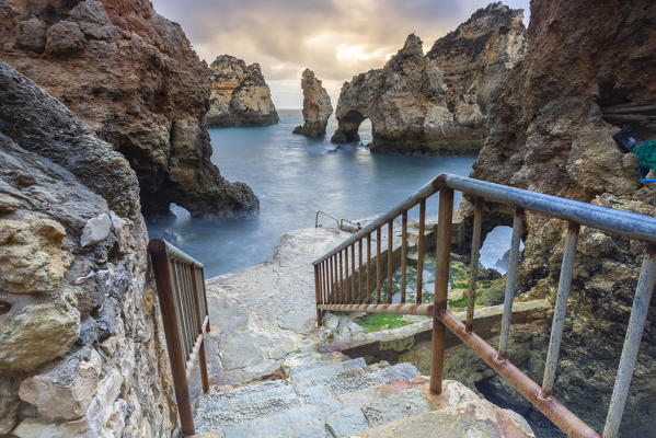 Banisters leading to the bottom of Ponta da Piedade during a cloudy sunrise. Lagos, Algarve, Portugal, Europe.