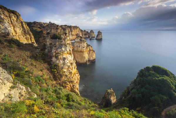 Cloudy sunrise at the yellow and red cliffs of Ponta da Piedade. Lagos, Algarve, Portugal, Europe.