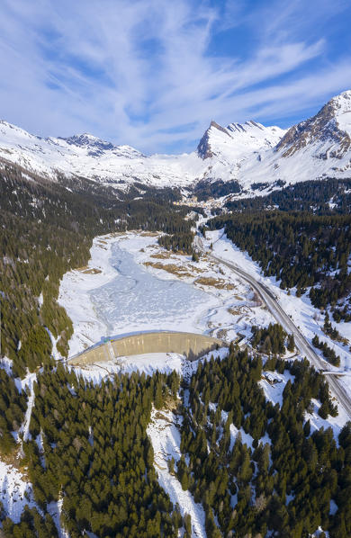 Aerial view of the iced Lago d'Isola lake and dam, and San Bernardino Pass road. Graubünden, Moesa district, Switzerland, Europe.