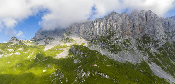Aerial view of the Presolana covered in clouds and the Città di Clusone bivouac at it's foothills. Passo della Presolana, Castione della Presolana, Val Seriana, Bergamo district, Lombardy, Italy.