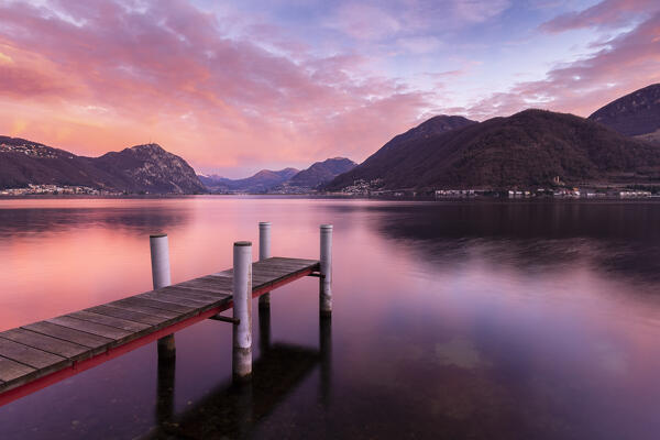 Sunrise explosion of colors in front of Lugano and Campione d'Italia from a pier on Lake Ceresio, Riva San Vitale, Canton Ticino, Switzerland.
