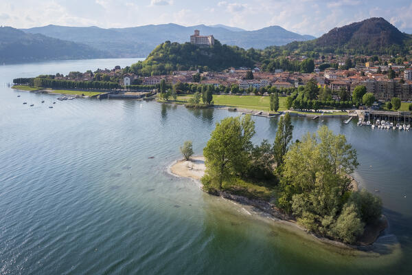 View of the town of Angera and its fortress called Rocca di Angera on a spring day with the small island called Isolino Partegora. Angera, Lake Maggiore, Varese district, Lombardy, Italy.