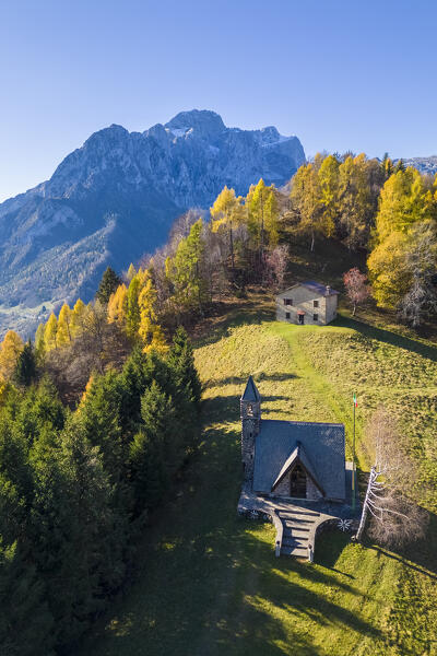 Aerial view of the small Alpini church of Azzone and the Presolana massif in autumn. Azzone, Scalve valley, Bergamo province, Lombardy, Italy.