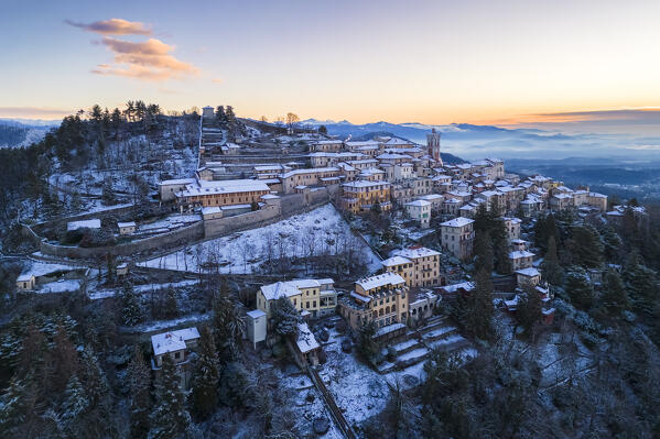 Aerial view of the town of Santa Maria del Monte after a snowfall in winter at sunrise. Varese, Parco Campo dei Fiori, Lombardy, Italy.