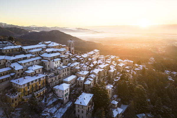 Aerial view of the town of Santa Maria del Monte after a snowfall in winter at sunrise. Varese, Parco Campo dei Fiori, Lombardy, Italy.