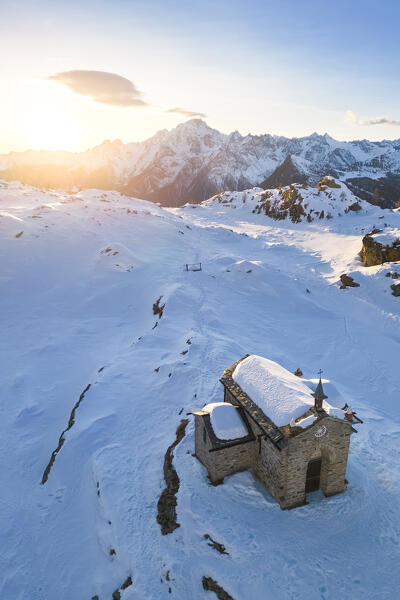 Sunset at Alpe Prabello with Santuario Madonna della Pace and Mount Disgrazia in the background in winter. Lanzada, Valmalenco, Valtellina, Sondrio district, Lombardy, Italy, Europe.