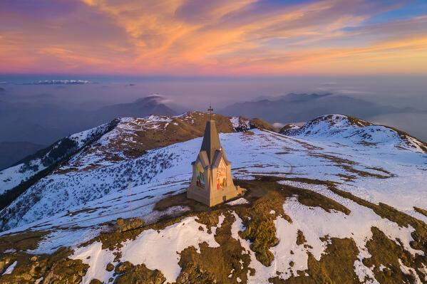 Aerial view of a winter sunset over Monumento al Redentore chapel on the top of Mount Mount Guglielmo. Zone, Brescia province, Lombardy, Italy