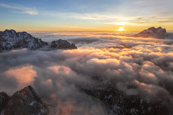 Aerial view of the Presolana mount at sunset in winter from above the clouds. Schilpario, Val di Scalve, bergamo district, Lombardy, Italy.