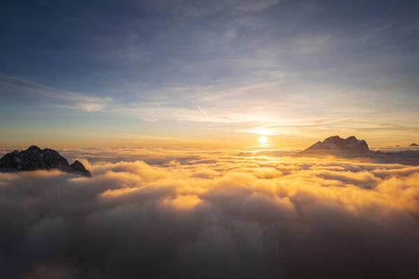 Aerial view of the Presolana mount at sunset in winter from above the clouds. Schilpario, Val di Scalve, bergamo district, Lombardy, Italy.