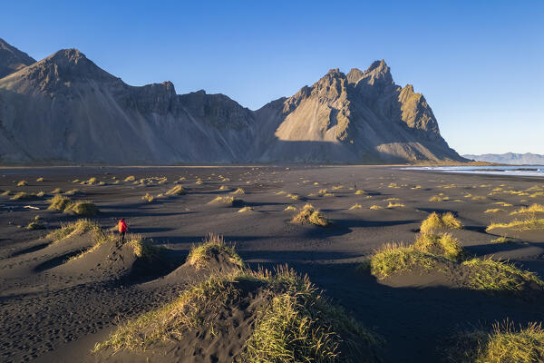 Aerial view of a person admiring the black sand dunes in front of Vestrahorn mountain at sunset. Stokksnes peninsula, Hofn, Austurland, Iceland, Europe.