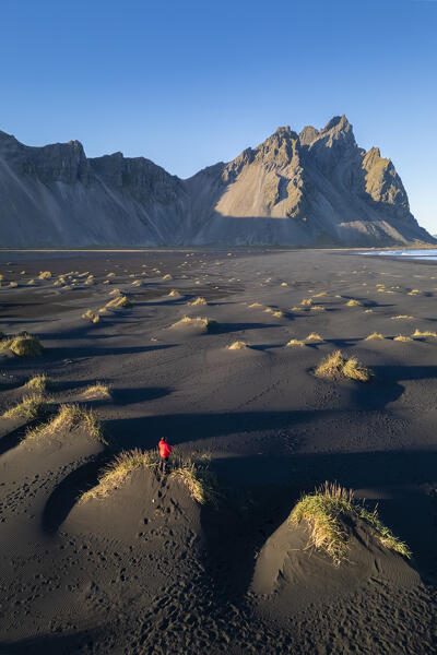 Aerial view of a person admiring the black sand dunes in front of Vestrahorn mountain at sunset. Stokksnes peninsula, Hofn, Austurland, Iceland, Europe.