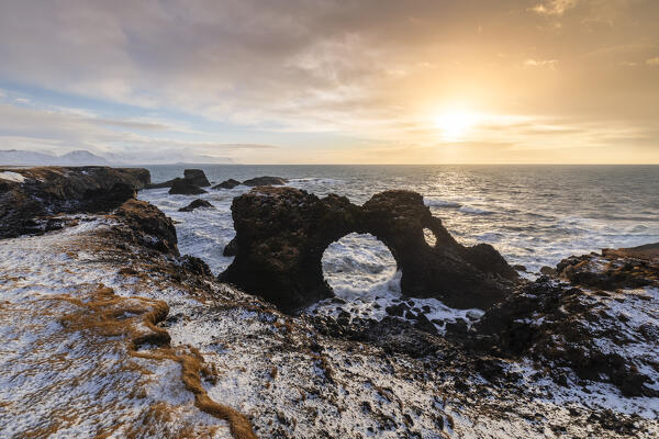View of the Gatklettur rock arch at sunrise in winter. Arnarstapi, Hellnar, Snæfellsnes Peninsula, Iceland, Northern Europe.