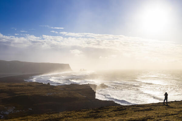View of a tourist taking photos at the sea stacks near Reynisfjara beach during sunrise in winter from Dyrholaey. Vík í Mýrdal, southern Iceland, Iceland, Northern Europe.
