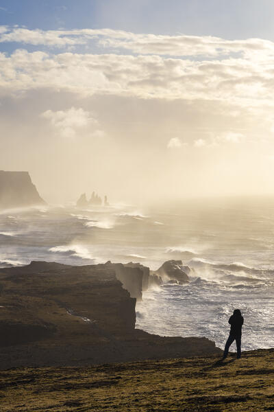 View of a tourist taking photos at the sea stacks near Reynisfjara beach during sunrise in winter from Dyrholaey. Vík í Mýrdal, southern Iceland, Iceland, Northern Europe.
