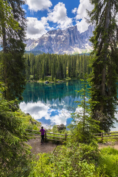 View of a girl admiring the Karersee lake in summer. Carezza, Dolomites, South Tyrol, Trentino Alto Adige, Italy. 