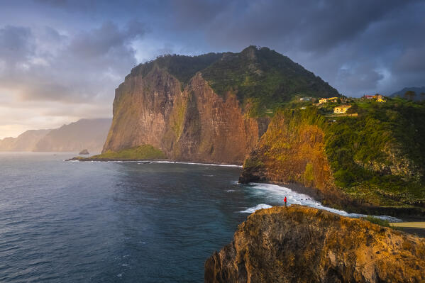 Aerial view of a tourist admiring sunrise from the cliffs of Miradouro do Guindaste. Madeira, Portugal, Europe.