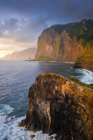 Aerial view of a tourist admiring sunrise from the cliffs of Miradouro do Guindaste. Madeira, Portugal, Europe.