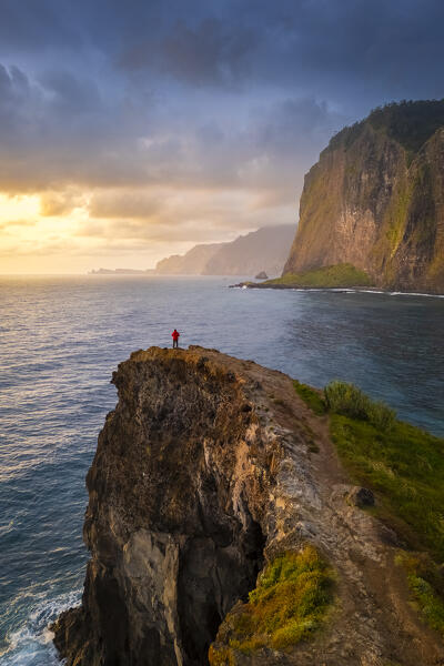 Aerial view of a tourist admiring sunrise from the cliffs of Miradouro do Guindaste. Madeira, Portugal, Europe.