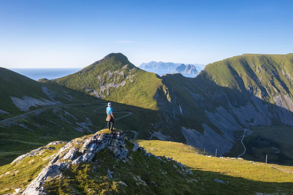Aerial view of a men admiring from a viewpoint the road to Haheia and the Lofoten islands in the background. Sorland, Vaeroy, Nordland, Lofoten, Norway, Europe.