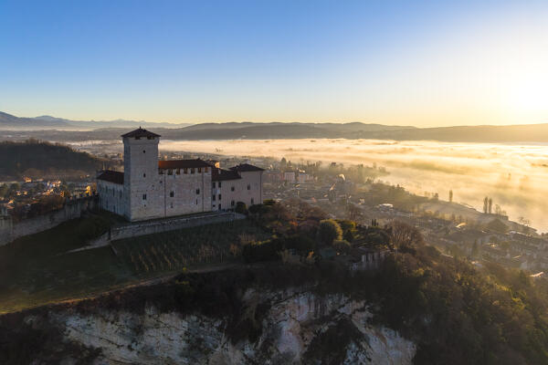 Aerial view of the fortress called Rocca di Angera during a winter sunrise surrounded by mist. Angera, Lake Maggiore, Varese district, Lombardy, Italy.