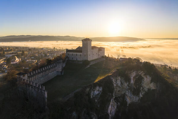Aerial view of the fortress called Rocca di Angera during a winter sunrise surrounded by mist. Angera, Lake Maggiore, Varese district, Lombardy, Italy.