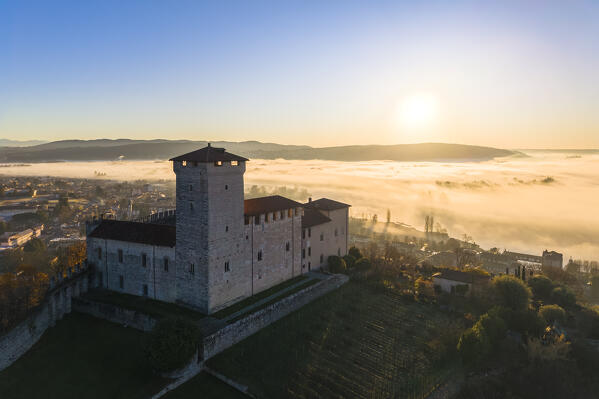 Aerial view of the fortress called Rocca di Angera during a winter sunrise surrounded by mist. Angera, Lake Maggiore, Varese district, Lombardy, Italy.
