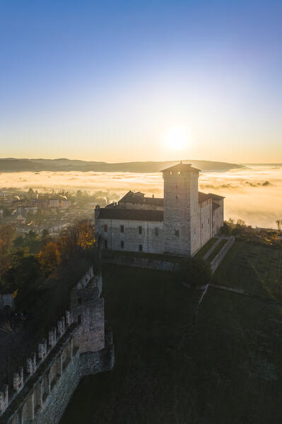 Aerial view of the fortress called Rocca di Angera during a winter sunrise surrounded by mist. Angera, Lake Maggiore, Varese district, Lombardy, Italy.