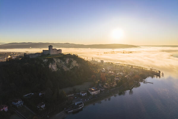 Aerial view of the fortress called Rocca di Angera during a winter sunrise surrounded by mist. Angera, Lake Maggiore, Varese district, Lombardy, Italy.
