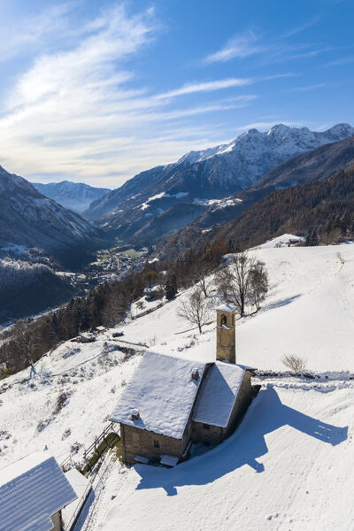 Aerial view of the church of Ripa di Gromo and the valley below after a snowfall in winter. Gromo, Val Seriana, Bergamo province, Lombardy, Italy, Europe.