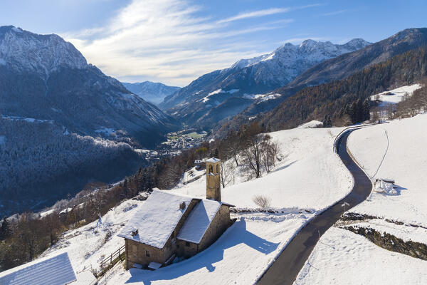 Aerial view of the church of Ripa di Gromo and the valley below after a snowfall in winter. Gromo, Val Seriana, Bergamo province, Lombardy, Italy, Europe.