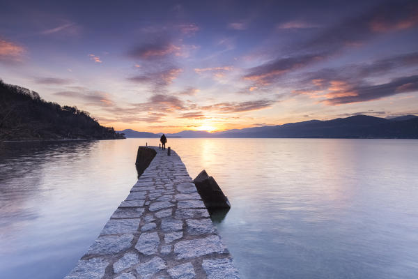 A lonely man staring at a colorful winter sunset at the old pier, Lake Maggiore, Ispra, Varese Province, Lombardy, Italy.