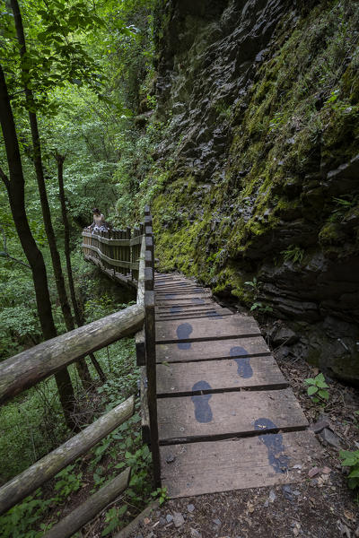 A girl walking on a wooden catwalk on the trail of the Breggia gorges, Muggio Valley, Mendrisio District, Canton Ticino, Switzerland.