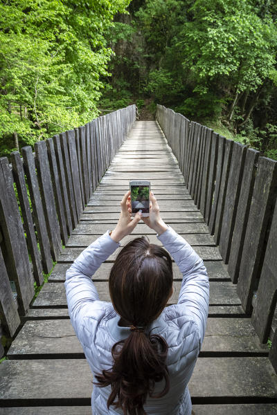 A girl taking a picture on a wooden bridge on the trail of the Breggia gorges, Muggio Valley, Mendrisio District, Canton Ticino, Switzerland.