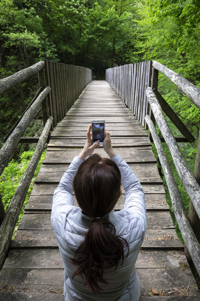 A girl taking a picture on a wooden bridge on the trail of the Breggia gorges, Muggio Valley, Mendrisio District, Canton Ticino, Switzerland.