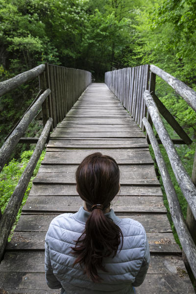 A girl crossing a wooden bridge on the trail of the Breggia gorges, Muggio Valley, Mendrisio District, Canton Ticino, Switzerland.