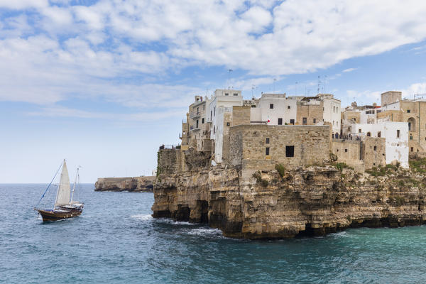 View of a ship sailing in front of the overhanging houses of Polignano a Mare. Bari district, Apulia, Italy, Europe.