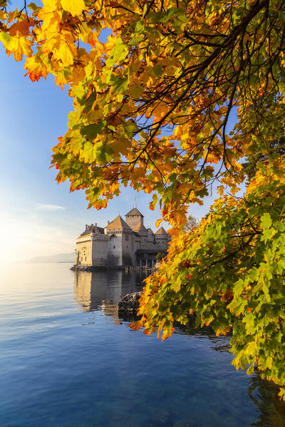 View of the Chillon castle on Lake Geneva surrounded by autumnal leaves at sunset. Veytaux, Montreux, Canton of Vaud, Switzerland.