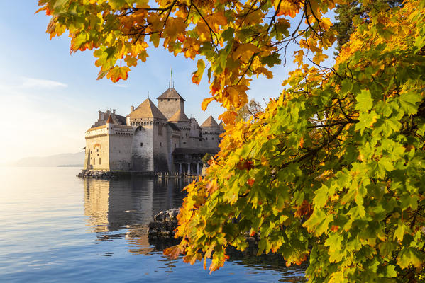View of the Chillon castle on Lake Geneva surrounded by autumnal leaves at sunset. Veytaux, Montreux, Canton of Vaud, Switzerland.