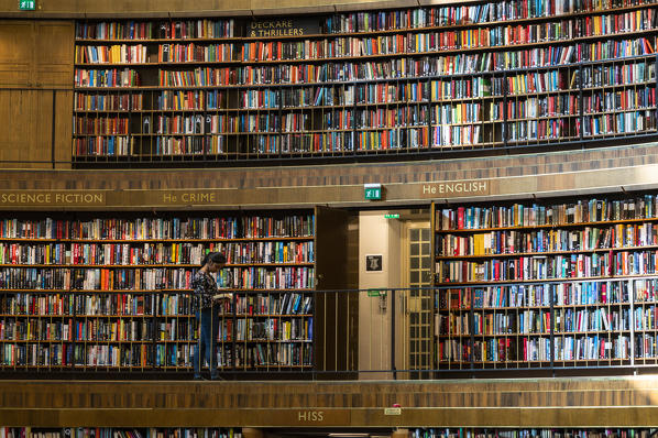 Woman reading a book standing beside the collections on shelves, Stadsbiblioteket, Stockholm public library, Sweden