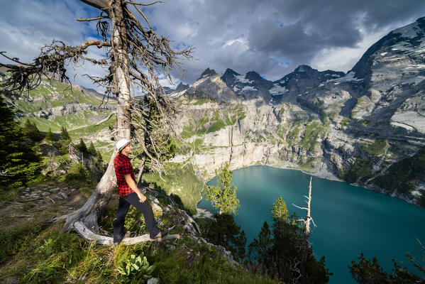 Side view of man leaning on tree trunk above Oeschinensee lake, Bernese Oberland, Kandersteg, Canton of Bern, Switzerland